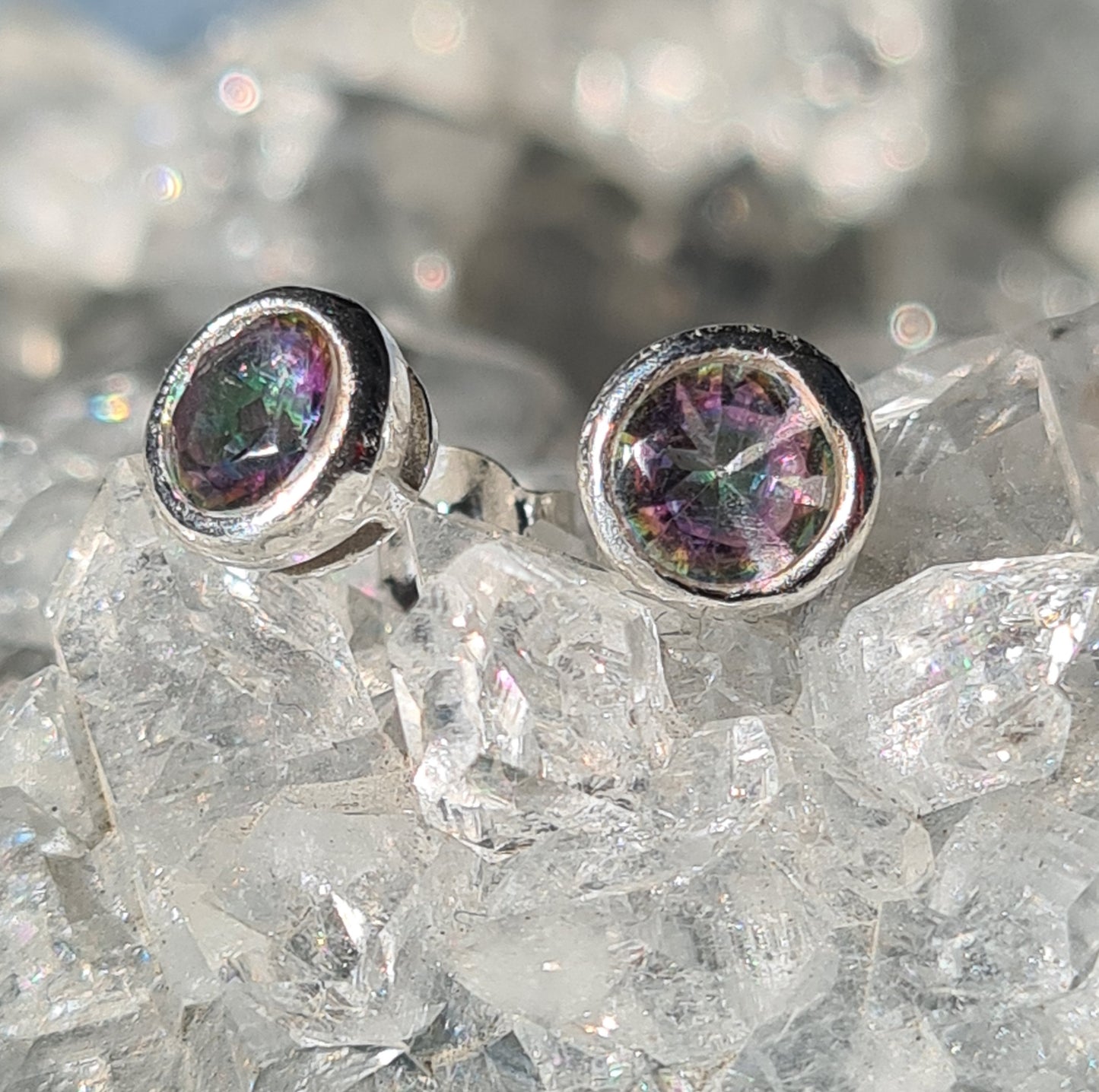 A pair of faceted mystic topaz set stud earrings in sterling silver. Shown on crystallised background.