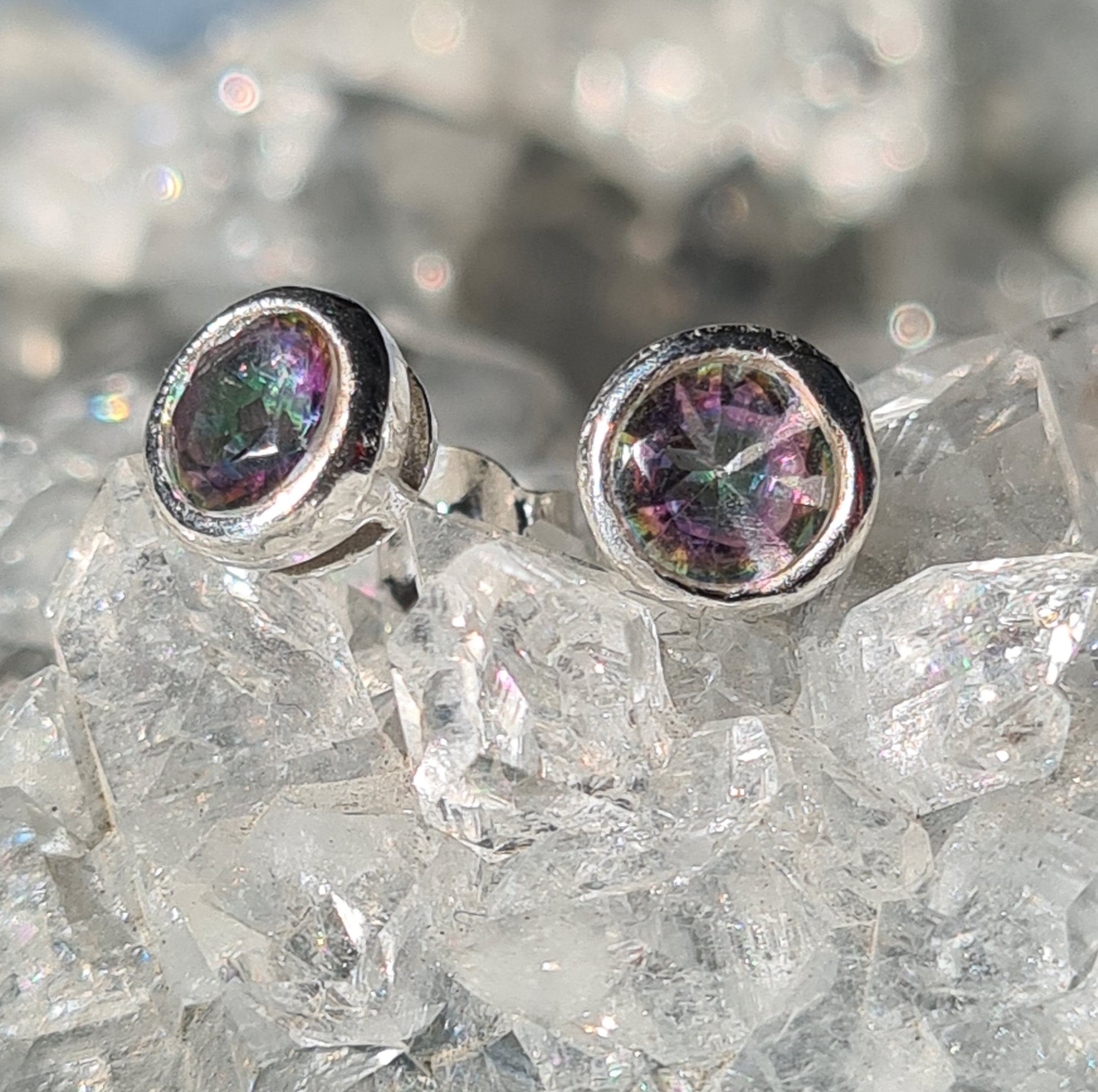 A pair of faceted mystic topaz set stud earrings in sterling silver. Shown on crystallised background.