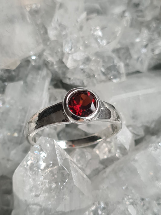 A round faceted garnet, rubover set in a bezel setting, with D-shaped shoulders and shank. Sizes J1/2, L and R1/2 available.