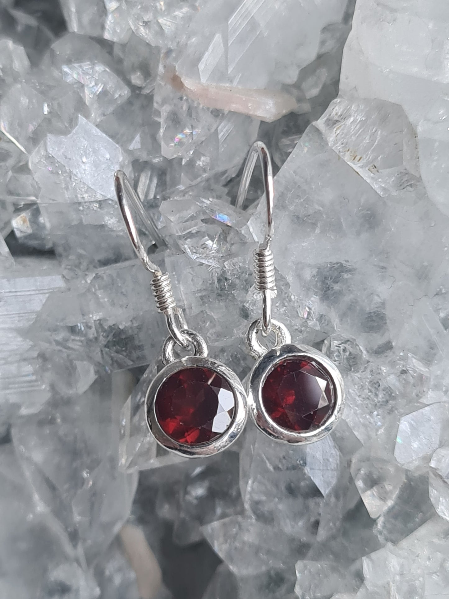 A pair of garnet set drop earrings, with a round faceted red garnet measuring 6mm diameter, set into sterling silver