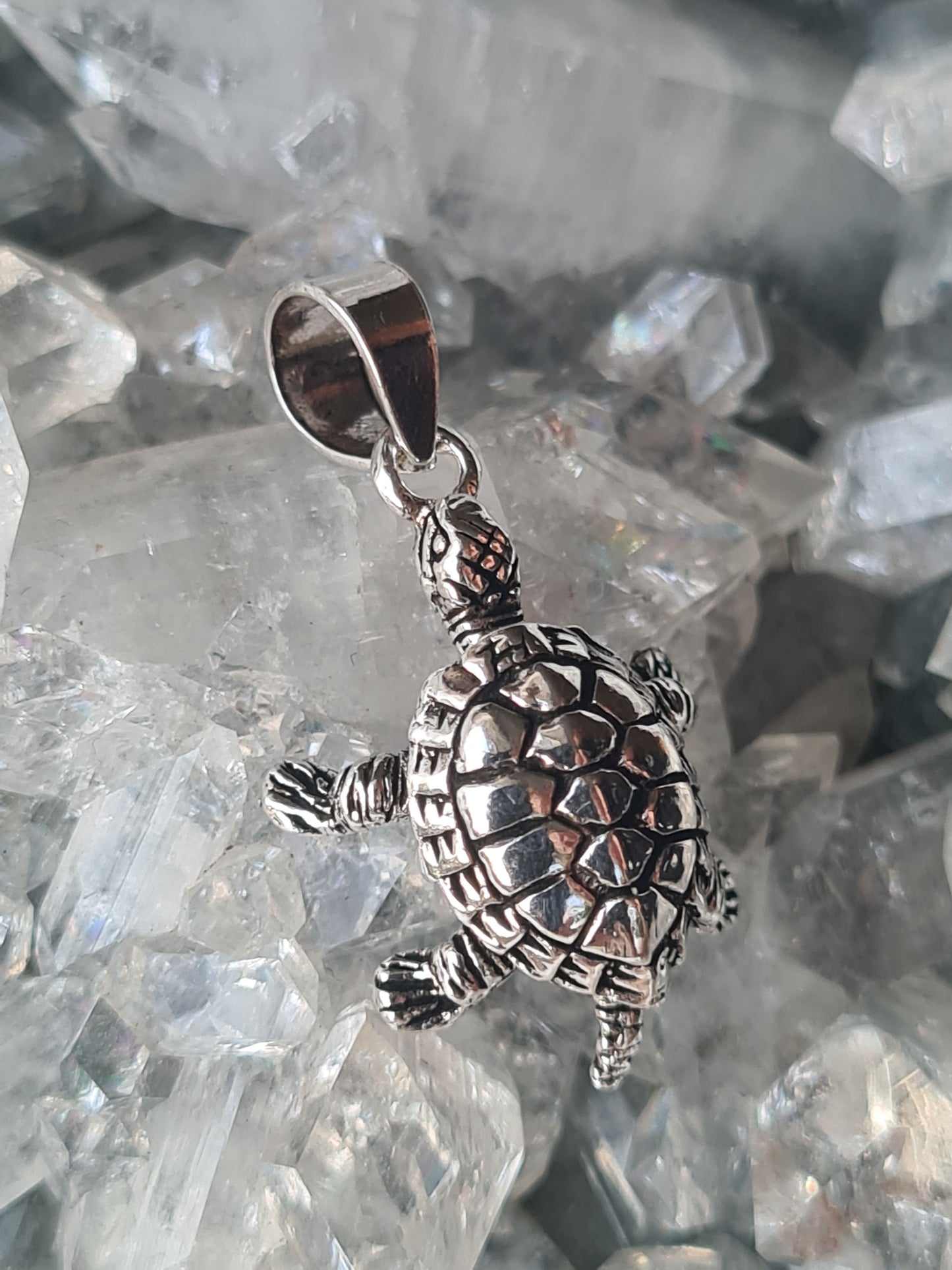 A sterling silver turtle pendant with articulating legs.
Photographed on a raw white crystal cluster.