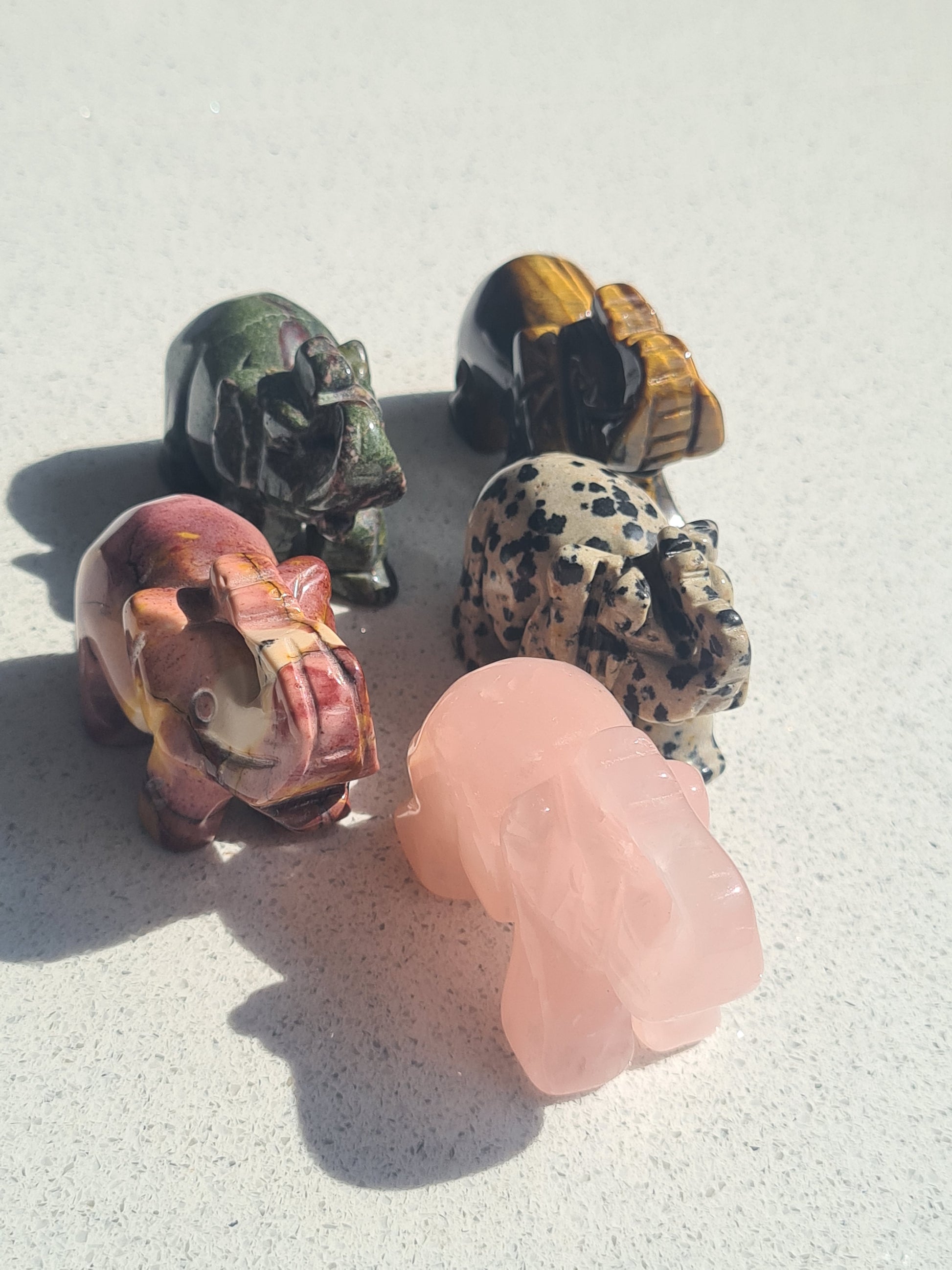 Collection of crystal elephant including rose quartz, Tigers Eye, Mookaite and bloodstone. Photographed on a white background. 