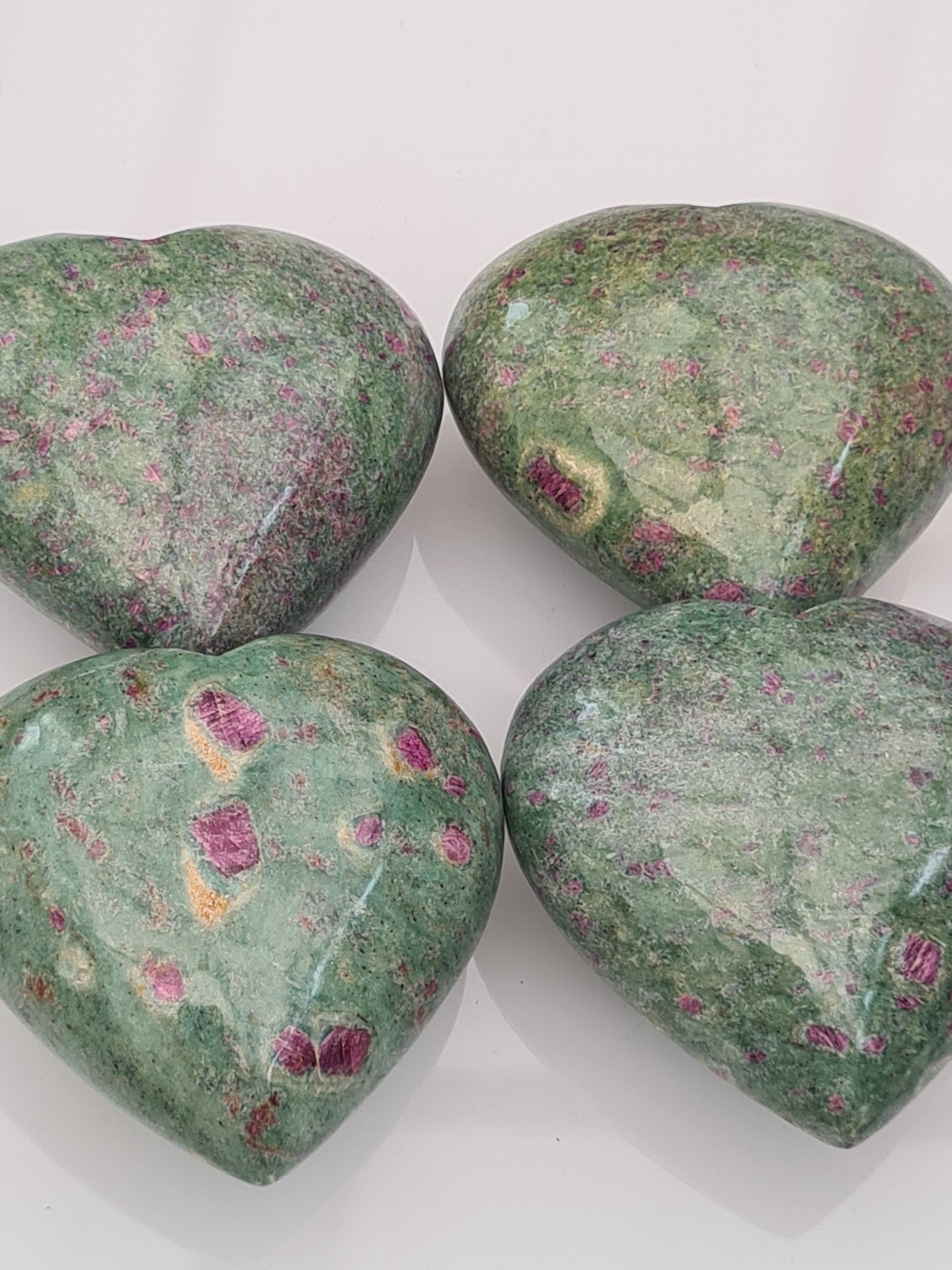 Four natural ruby in green fuchsite carved hearts on white background. 