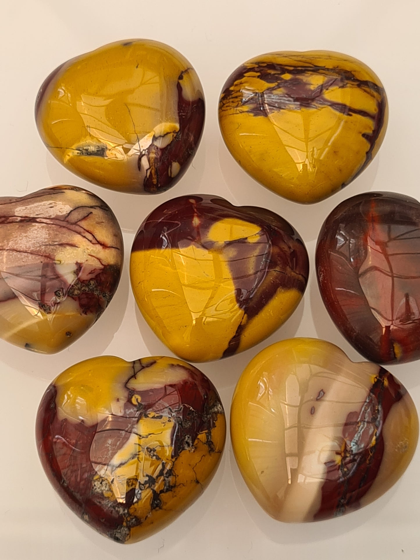 3cm Mookaite polished hearts, colours of yellow, red and pink. 7 shown on a white background.