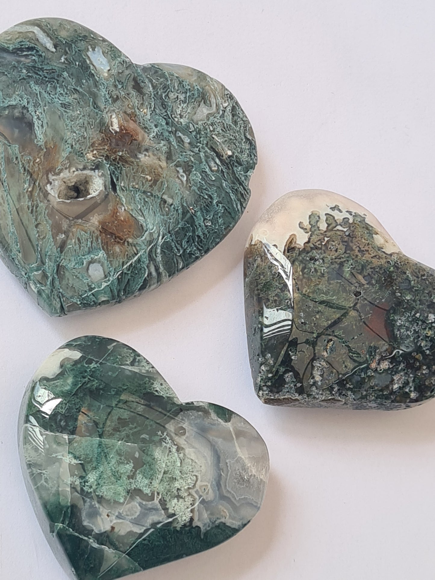 Three moss agate polished hearts, green included agate with chalcedony and caves. On a white background.