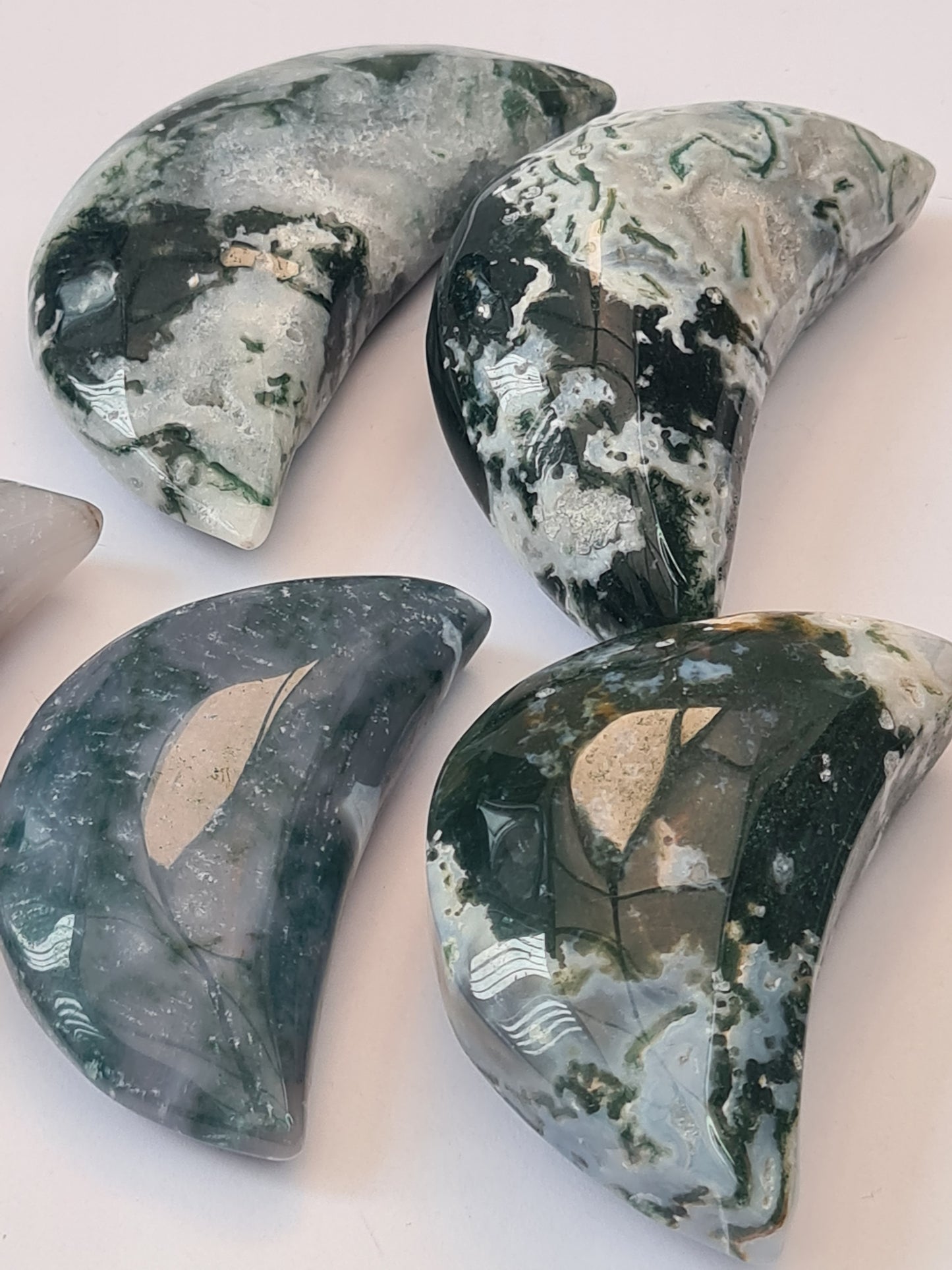 Moss Agate Crescent Moon Carvings. Green with blue and white chalcedony. Four shown on a white background.