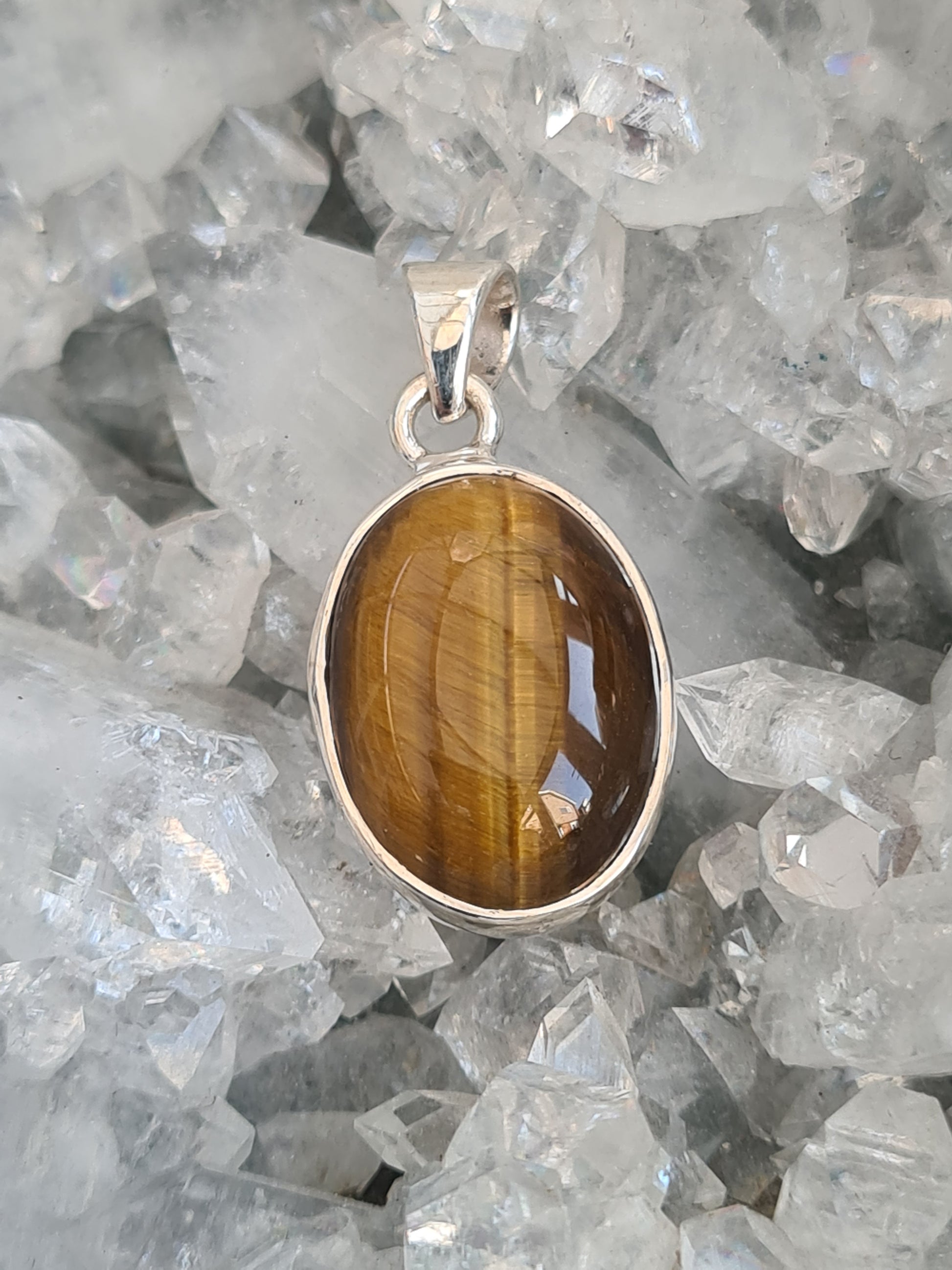 A golden tigers eye set pendant. Oval shaped cabochon, rubover set, in all Sterling Silver.
Photographed on a diamond apophyllite cluster. 