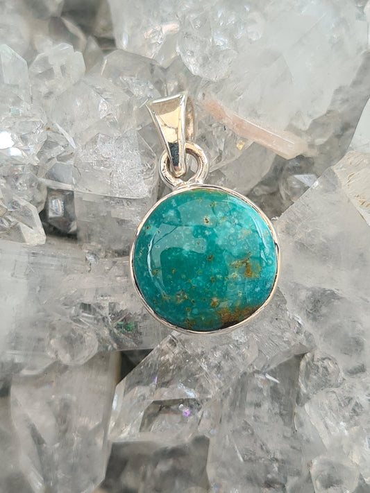 A round Turquoise set pendant in sterling silver. Vivid green/blue colour.
Photographed on a white apophyllite crystal background. 