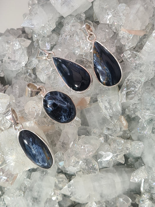 Collection of blue pietersite crystal set pendants in sterling silver. pictured on crystalline background.