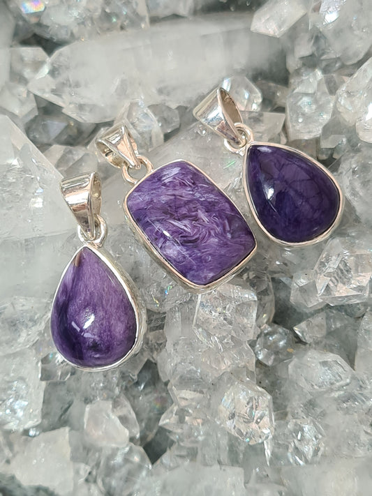 Three Natural Purple Charoite Pendants in Sterling Silver. Middle Cushion Shape, Both Outer are Pear Shaped.
Photographed on an apophyllite cluster background. 