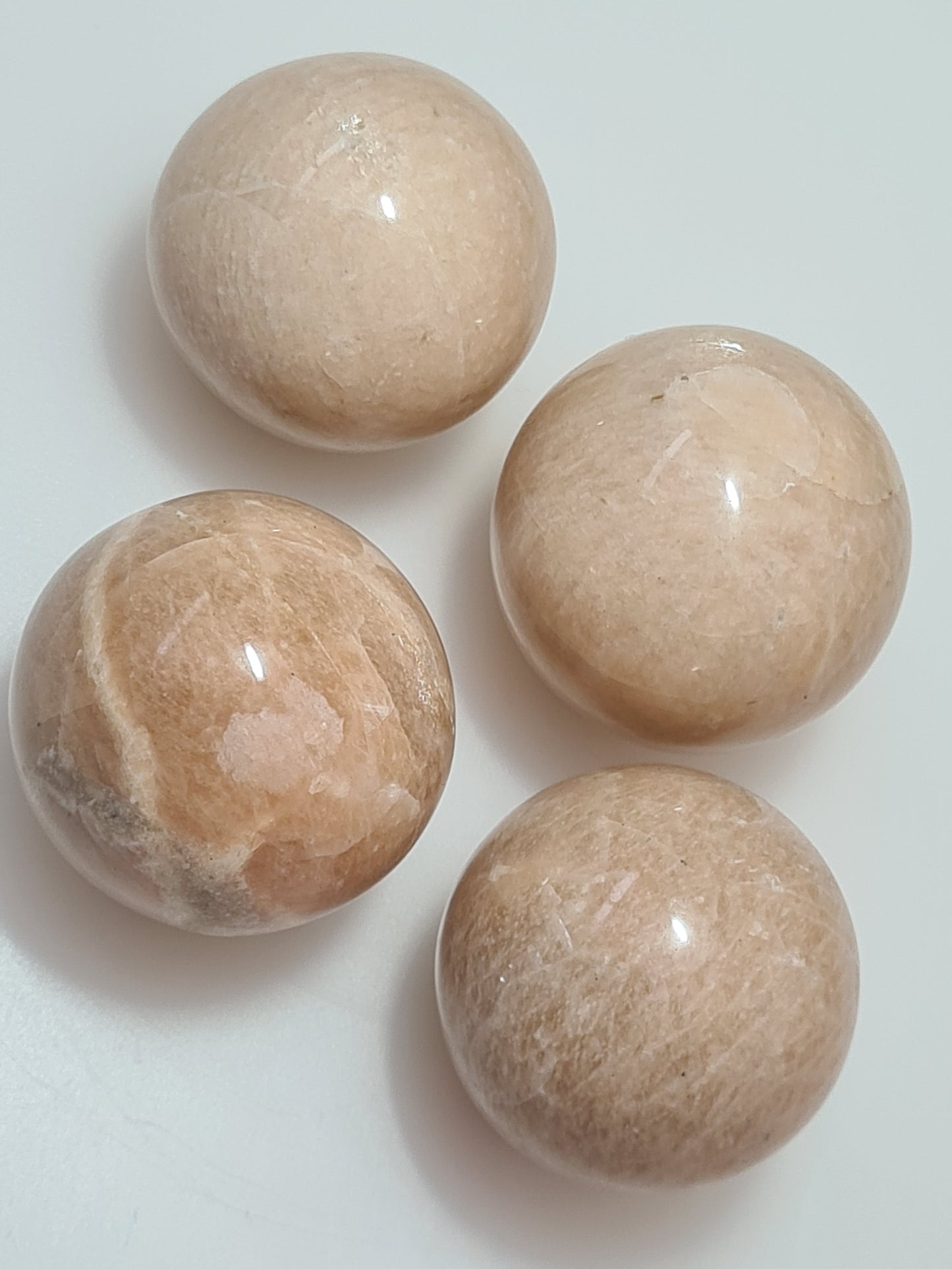 Collection of peach moonstone spheres, pale to medium colour, on white background. 