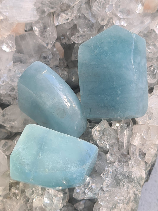 Natural Brazilian Aquamarine Polished Specimens in vivid aqua blue colour. 
Three pieces photographed on a raw crystal background. 
