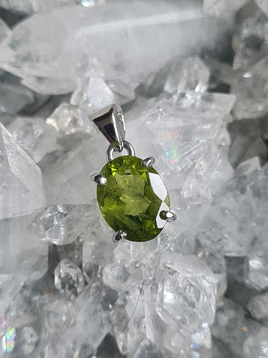 Natural Peridot set pendant in sterling silver. Faceted oval shaped green peridot in vivd lime colour. Four claw set, with articulating bail. 
Photographed on an apophyllite cluster background. 