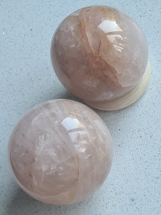 Pair of Natural Fire Rose Quartz Spheres in pink with orange/red inclusions of hematite.
Photographed on a white granite background. 