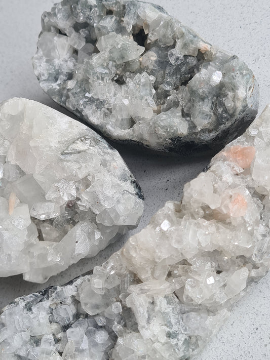 Collection of white apophyllite raw crystals. Diamond and cubic formations, some with peach Stilbite or red Heulandite. 
Photographed on a white background. 