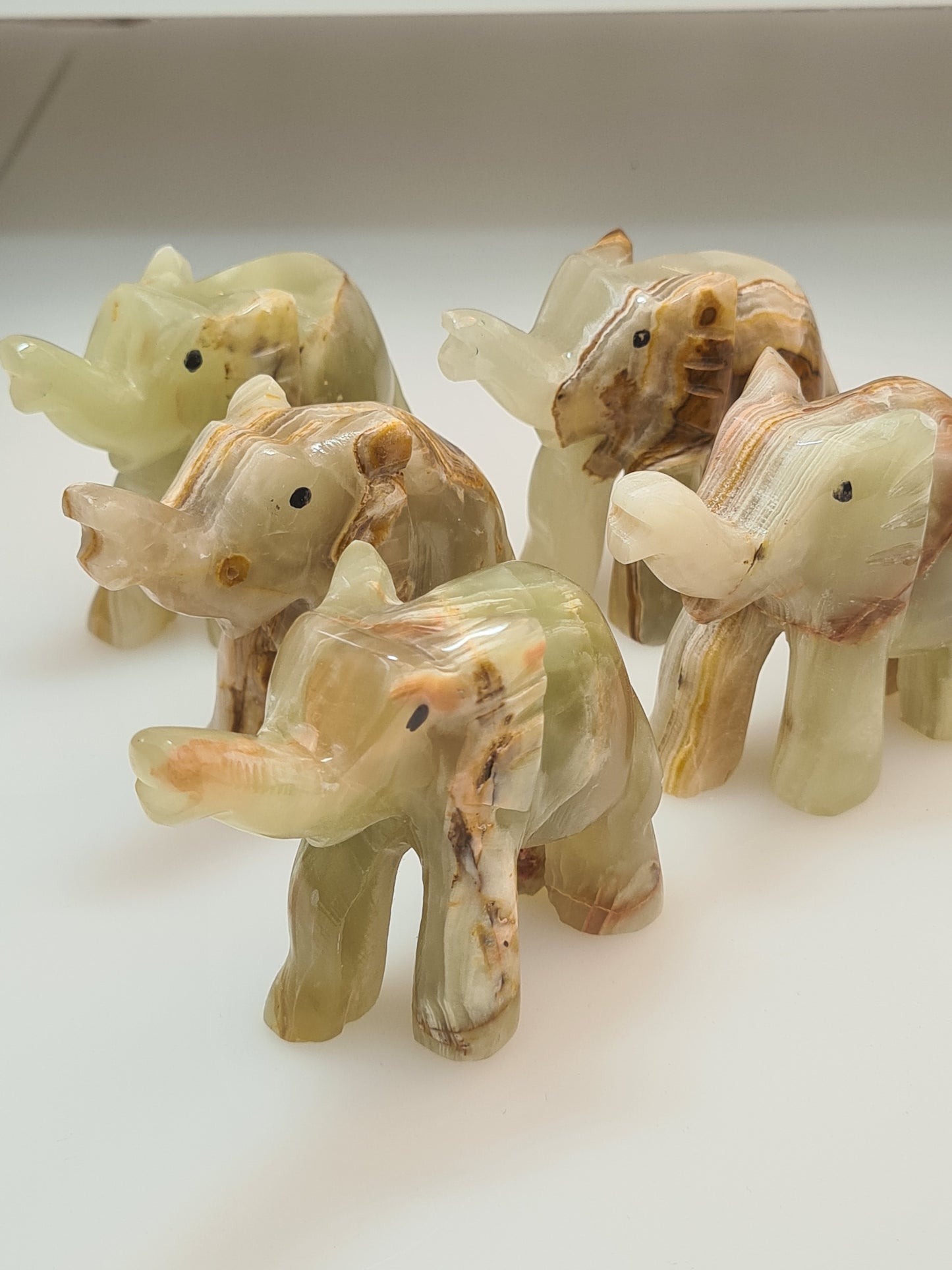 Banded calcite standing elephant carvings, in green with banding of white, yellow, orange and brown. Photographed on a white background. 