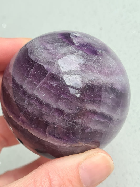 Natural Purple Silky Fluorite Sphere measuring 62mm diameter with purple and white banding. Small green area to one side. 