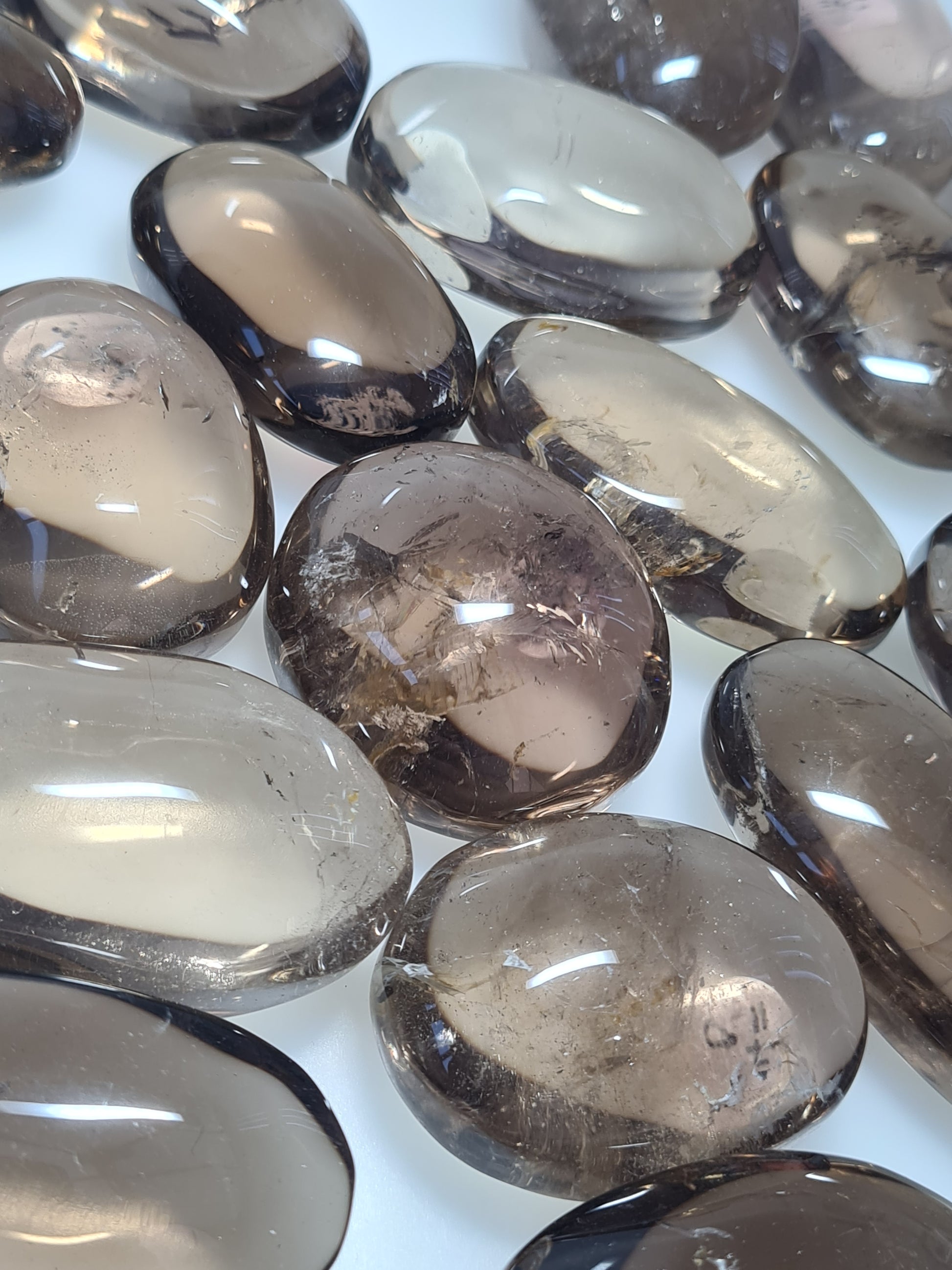 Collection of smoky Quartz oval shaped palmstones in different shades of brown. Photographed on a white background. 