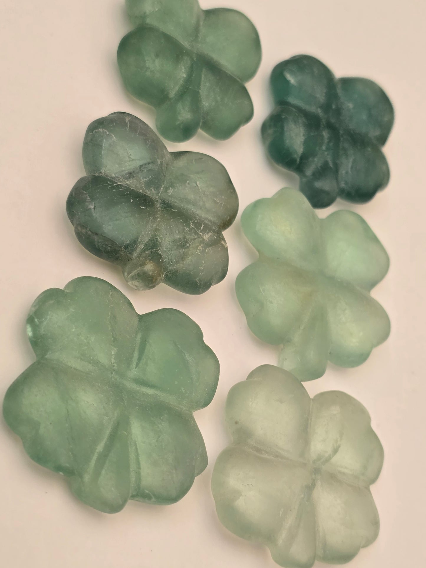 Six natural green fluorite crystals carved as a four leaf clover for luck and good fortune. Photographed on a white background. 