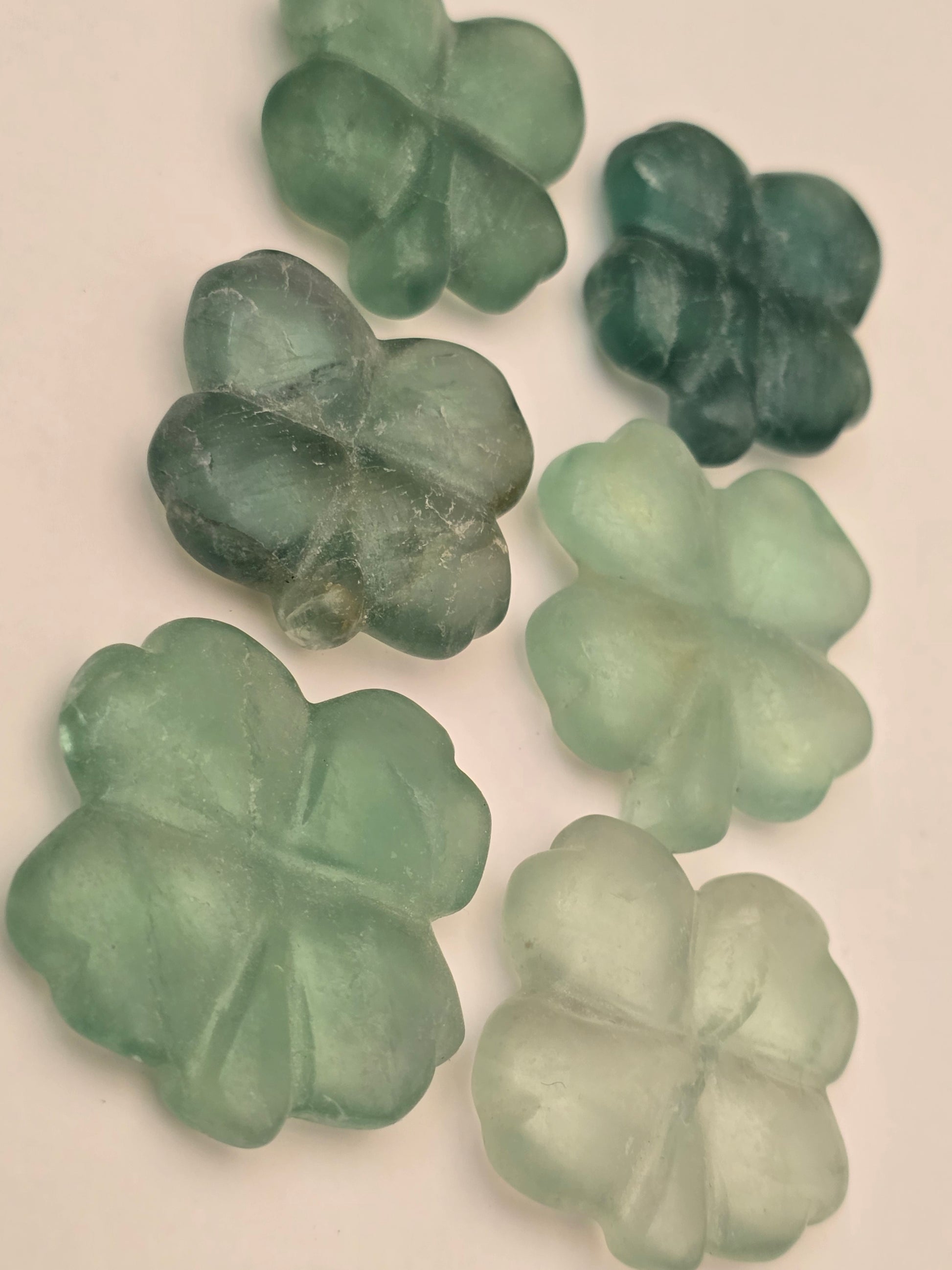 Six natural green fluorite crystals carved as a four leaf clover for luck and good fortune. Photographed on a white background. 