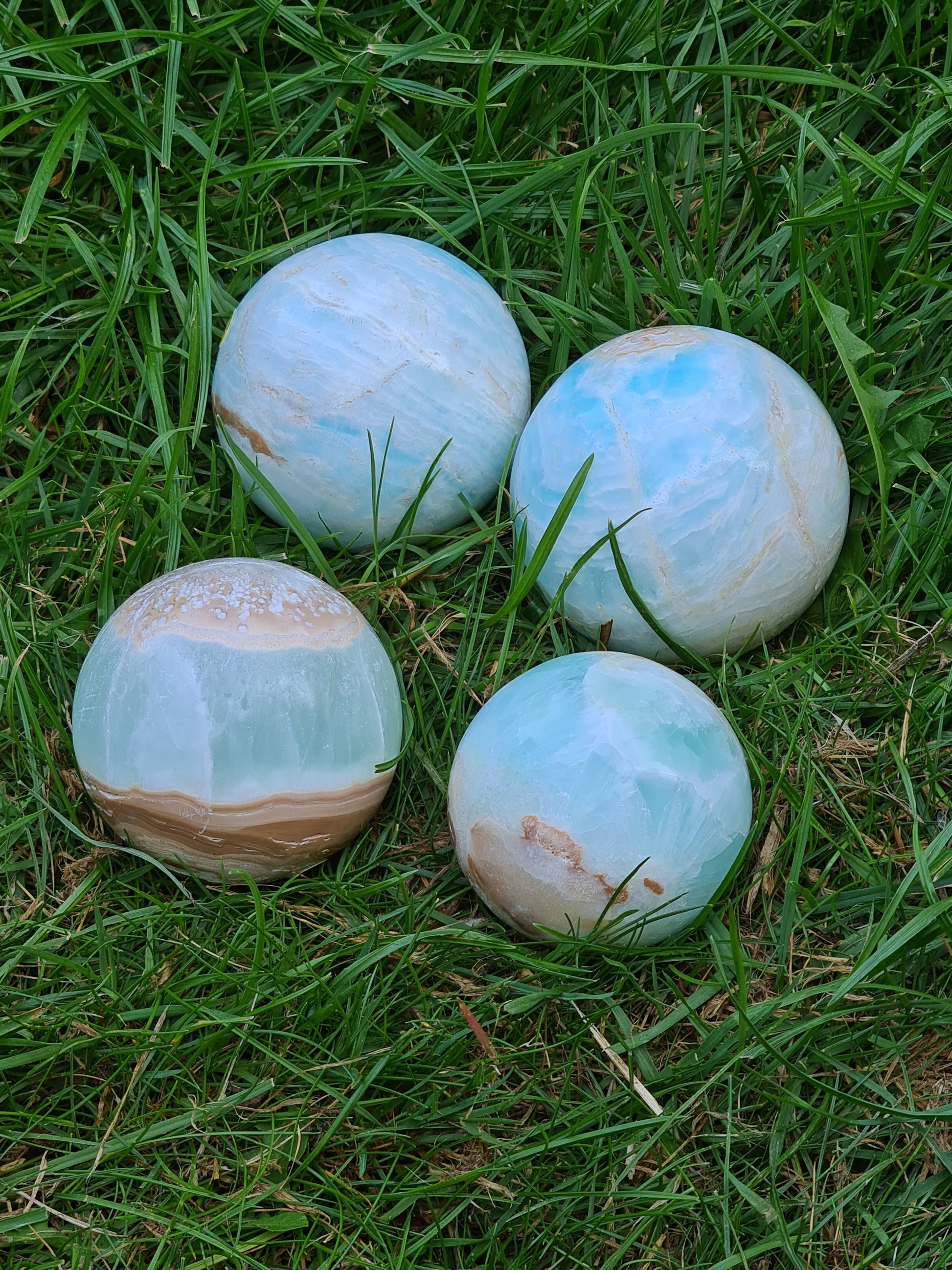 A collection of four Caribbean Calcite Spheres with sea blue calcite, white calcite and brown aragonite banding