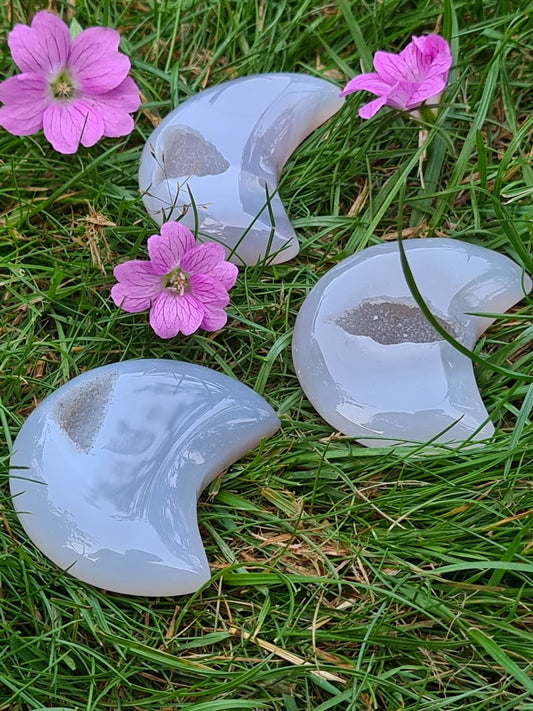 Three Druzy Agate Moons, grey in colour with central druzy quartz, photographed on grass with pink flowers
