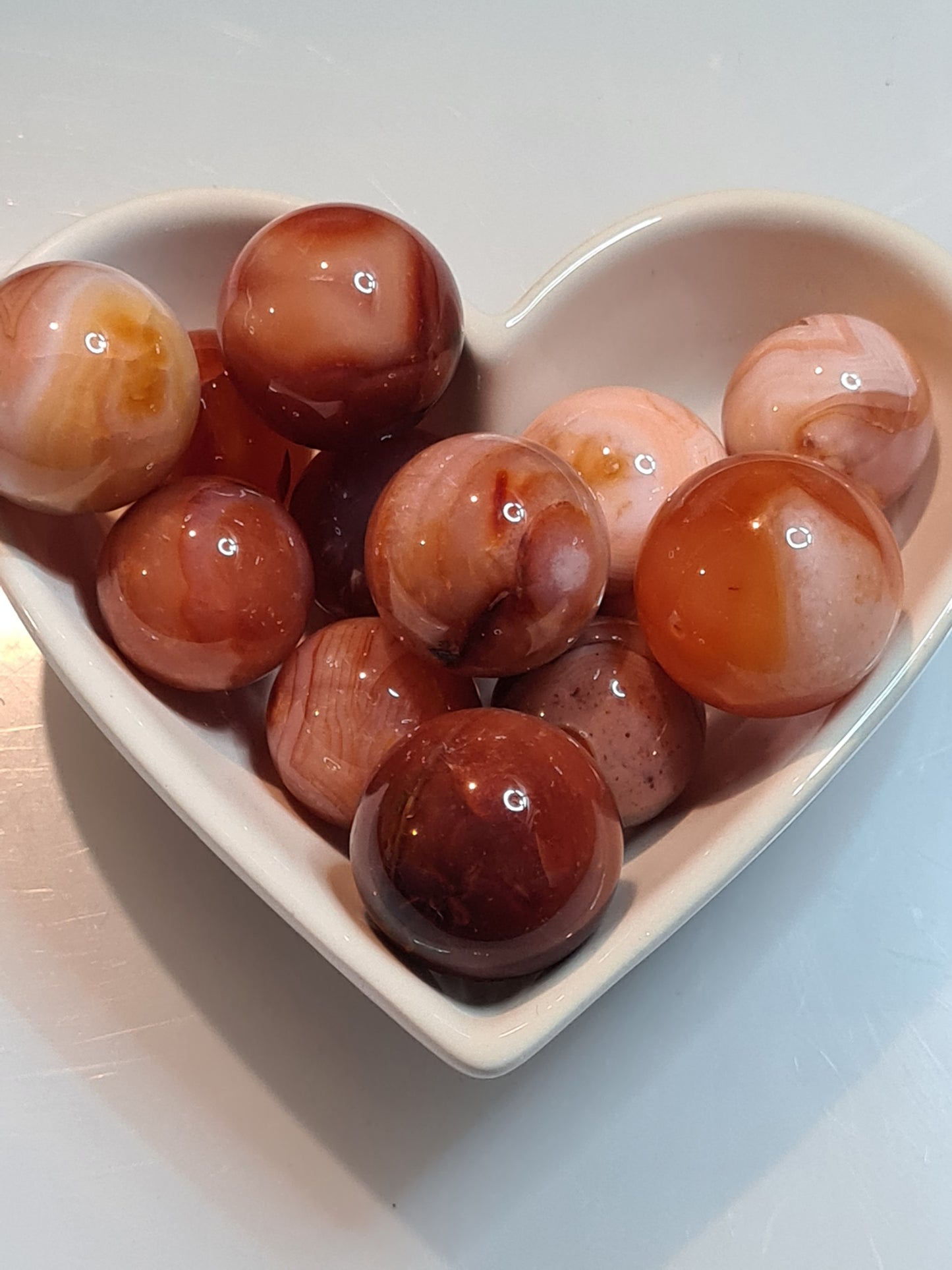 A heart shaped white bowl full of juicy orange and white banded Carnelian small spheres for motivation and energy