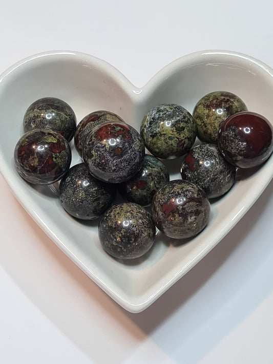 A white heart shaped bowl filled with small spheres of Bloodstone aka Heliotrope, made up of green jasper with 'blood' red inclusions of hematite