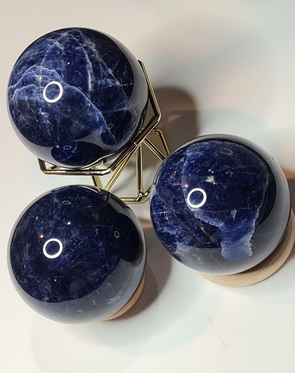 Three Polished Blue Sodalite Spheres, one sitting in a gold coloured metallic wire stand