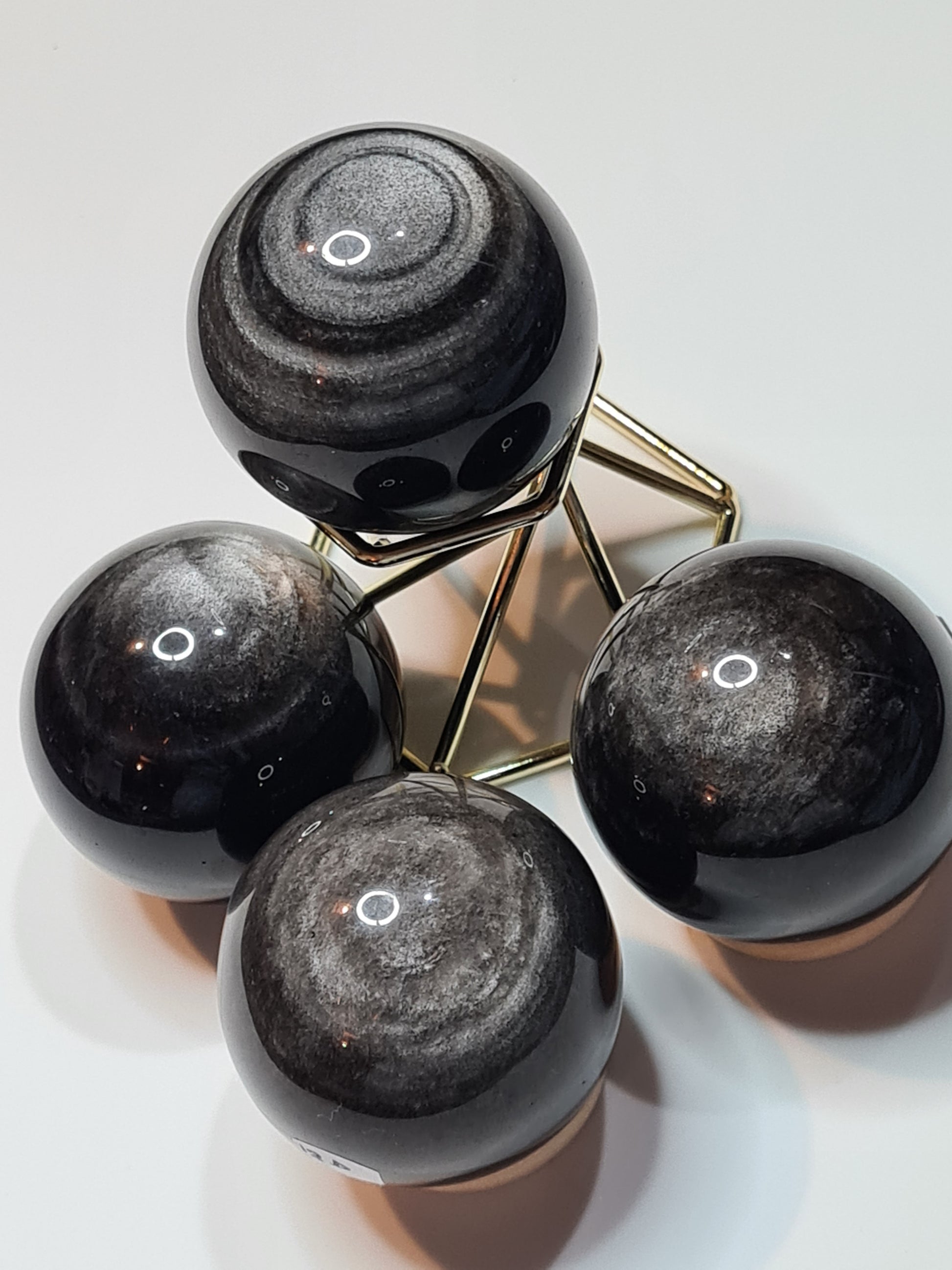 Four Shimmering Silver Sheen Obsidian Spheres with black bodycolour, one sitting on a gold coloured wire stand