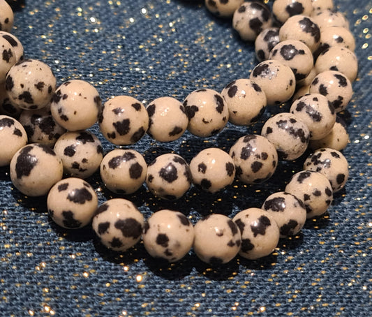 Natural Dalmatian jasper 6mm beaded bracelets, cream stone with black dot inclusions.
Photographed on a sparkly teal background. 