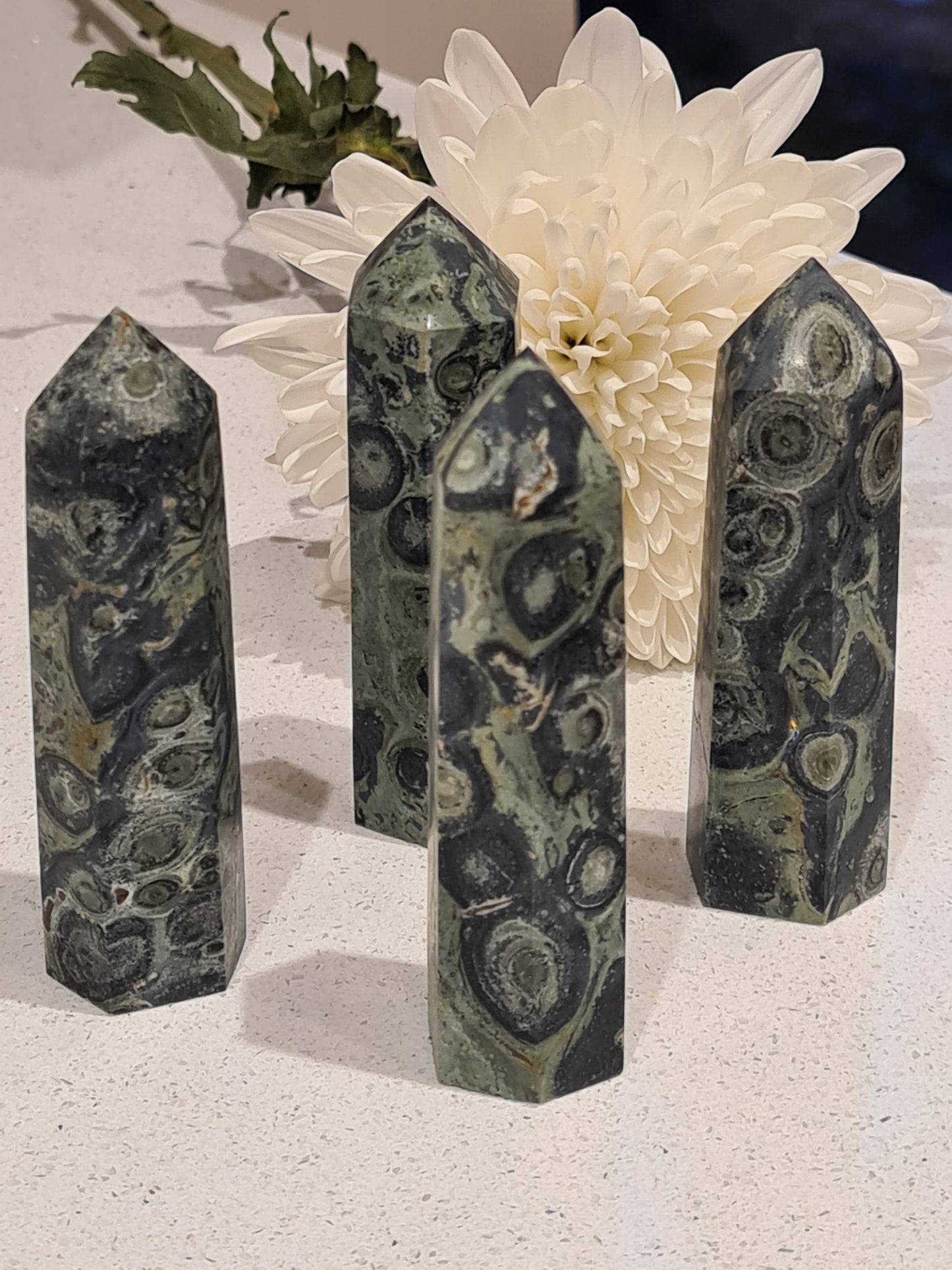 A collection of green, black and grey swirl Kambaba Jasper Towers, with a white Chrysanthenum flower in the background
