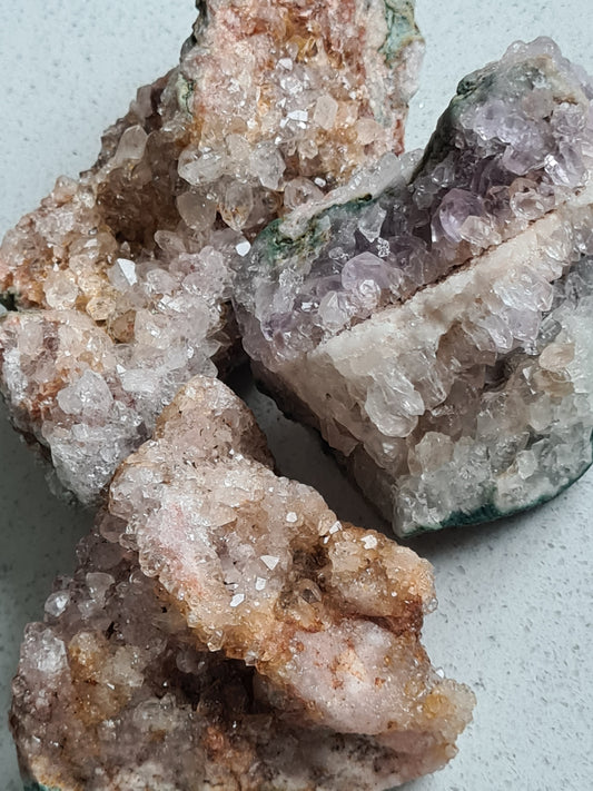 A collection of Pink Amethyst Raw Clusters from Brazil, colours of pink, white and yellow. on white quartz background.