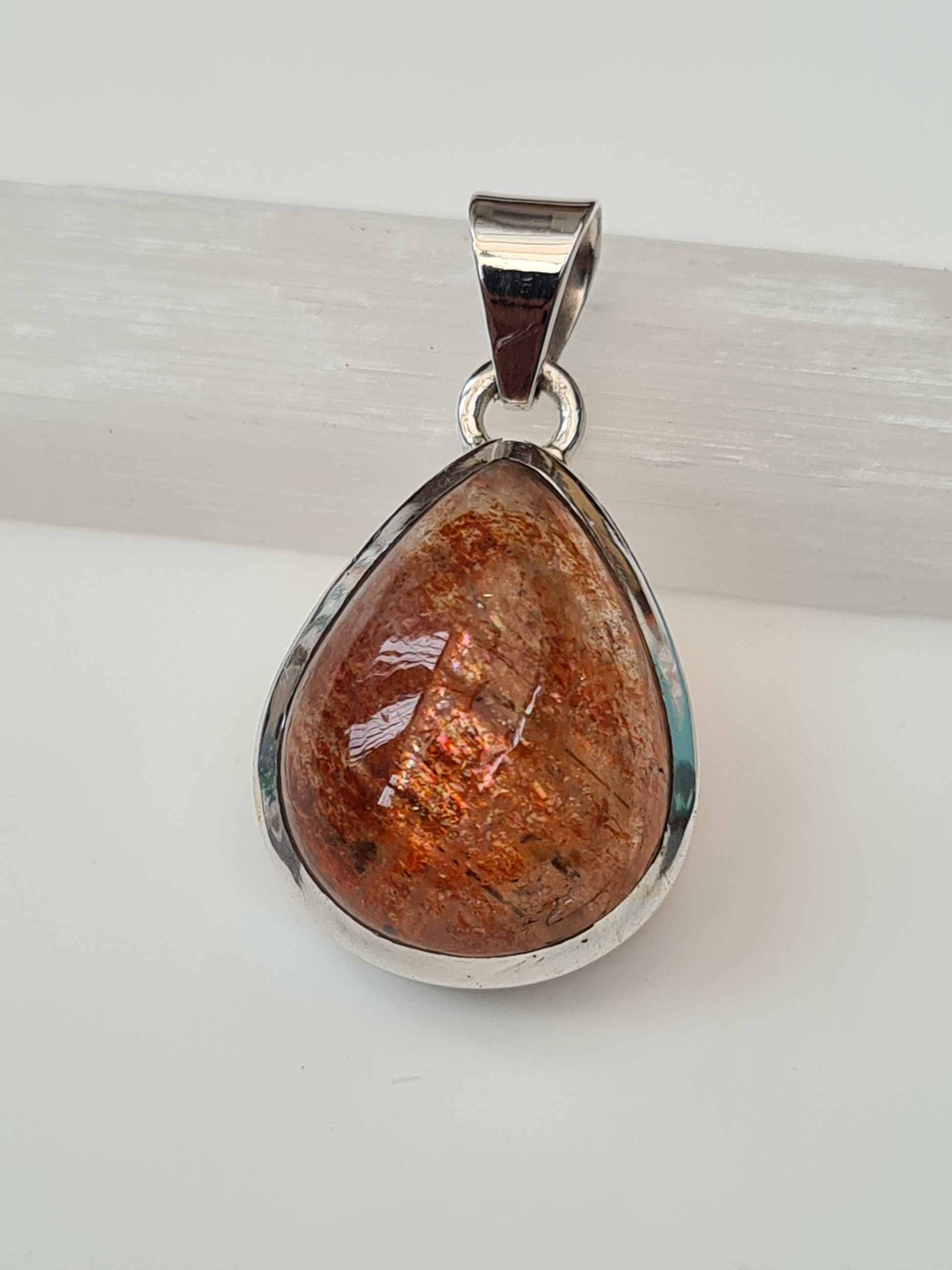 A sunstone single stone pendant in sterling silver. Natural orange pear shaped sunstone with colourful spangles. 
