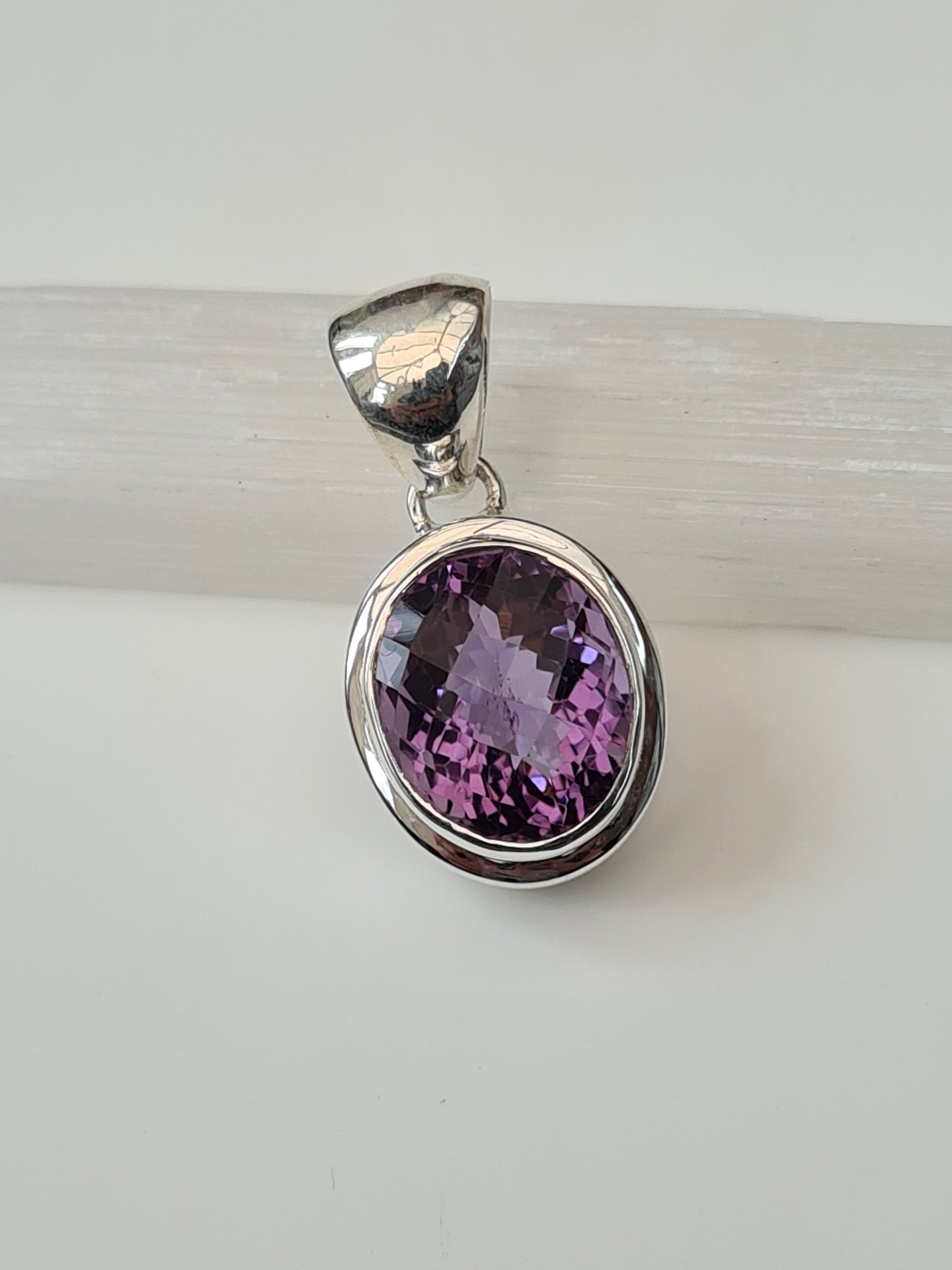 An Amethyst Pendant. Centring on a faceted oval amethyst rubover set to a bezel setting with articulating bail. 925 Sterling Silver