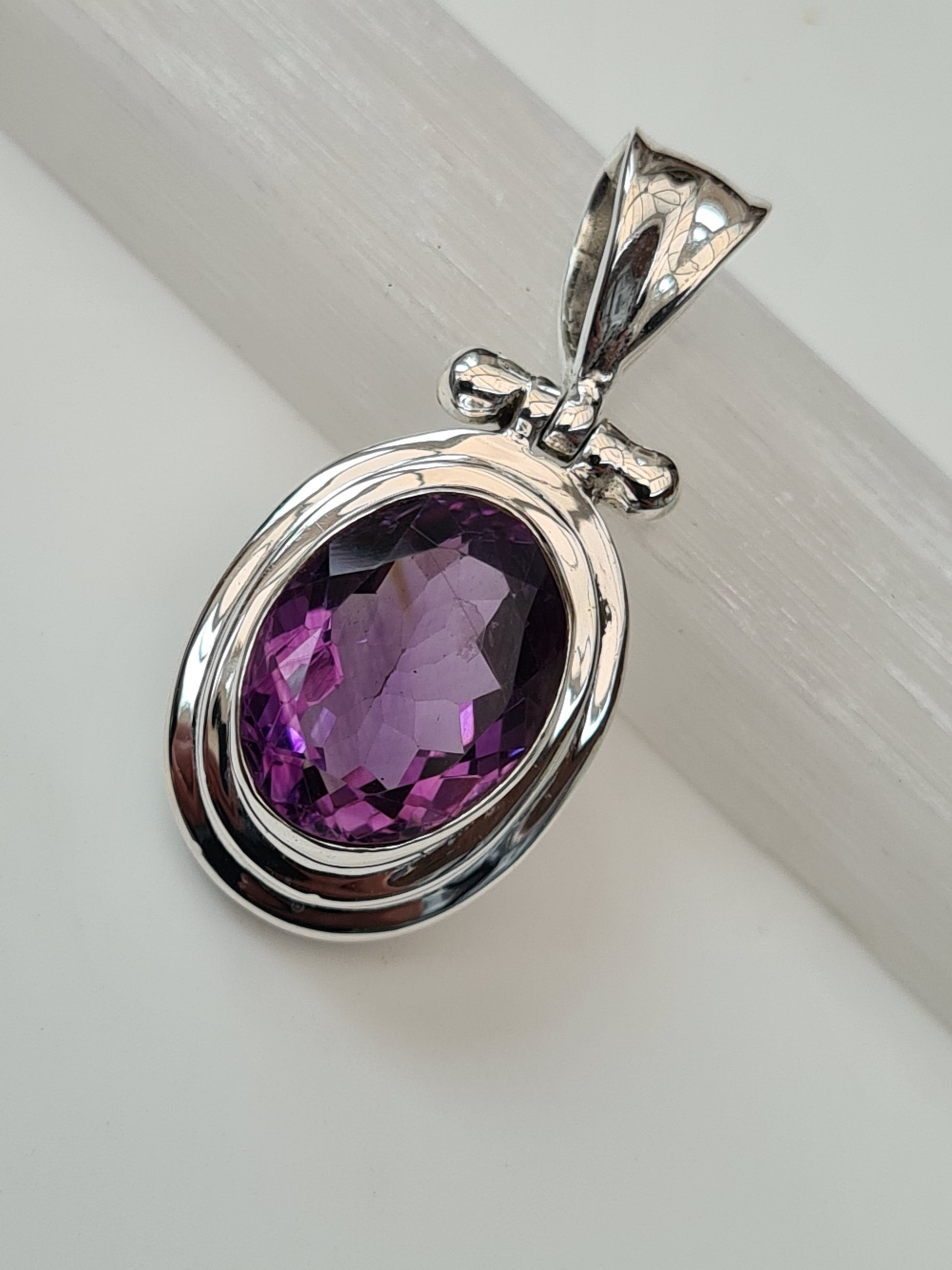 An Amethyst Pendant in Sterling Silver. With a central rubover set oval faceted amethyst, double row polished frame and articulating bail. 