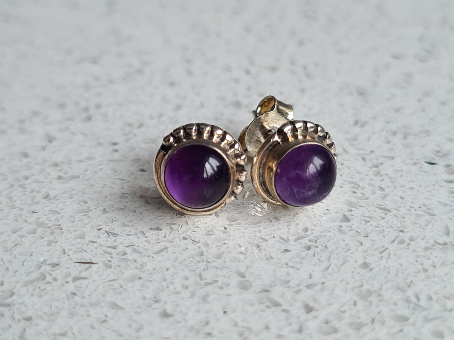 A pair of round cabochon amethyst set stud earrings with bead detail to the border.