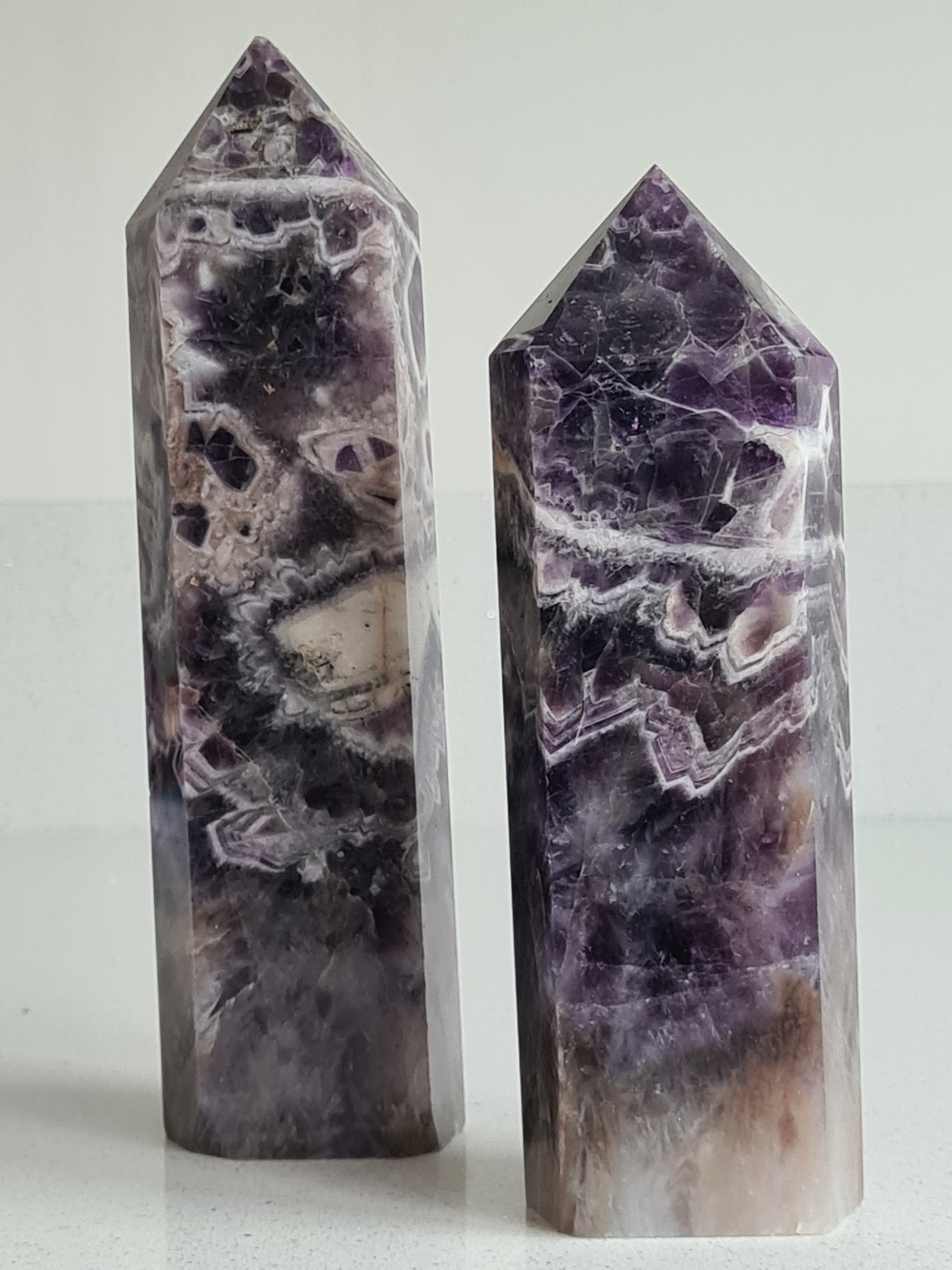 Two Large Dream Amethyst Towers, measuring one at 56cm, one at 55cm tall. Unique deep purple and white chevron banding with some smoky quartz sections