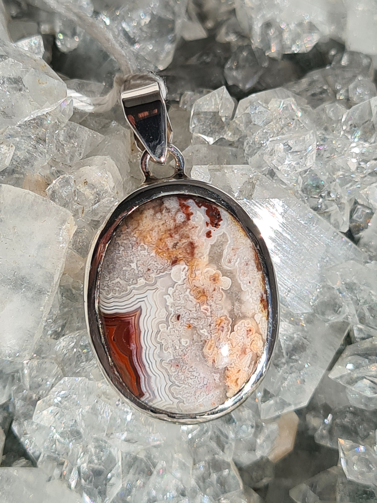 A Mexican Crazy Lace Agate Oval Cabochon, rubover set into a sterling silver frame. Colours of white, grey, orange and red in the stone