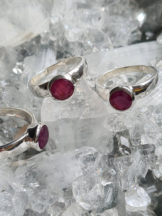 Collection of natural Indian untreated red ruby set rings in sterling silver. Three shown on a crystalline background. 
