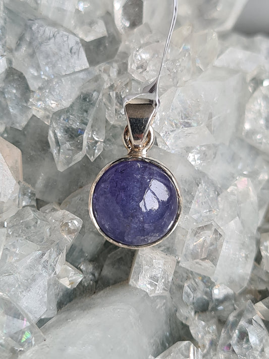 A round purple tanzanite pendant set in sterling silver. Crystal cluster background 