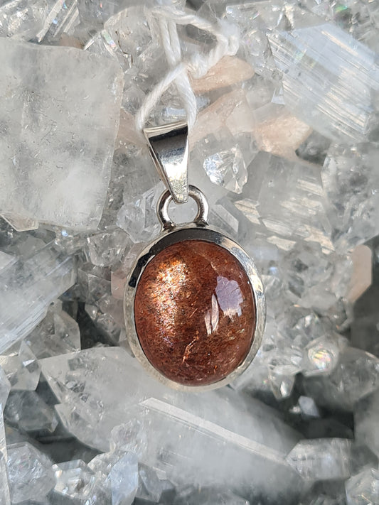 A natural orange sunstone pendant, featuring an oval cabochon sunstone with colourful spangles, set into sterling silver 