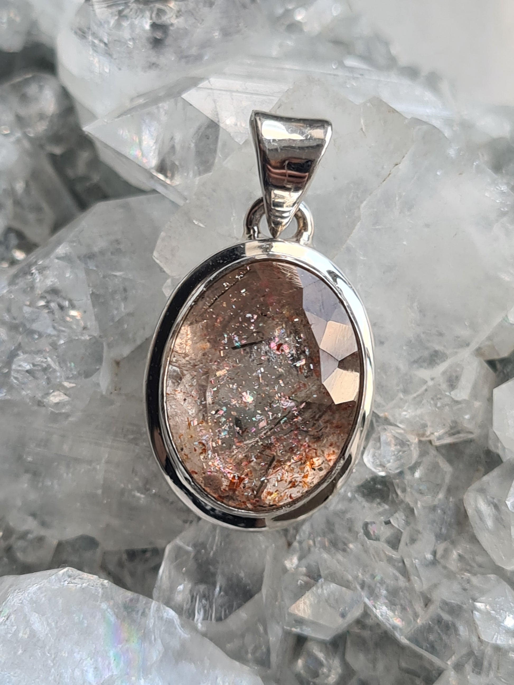 Natural faceted Oregon sunstone pendant, rubover set in sterling silver. Photographed on a crystal background.