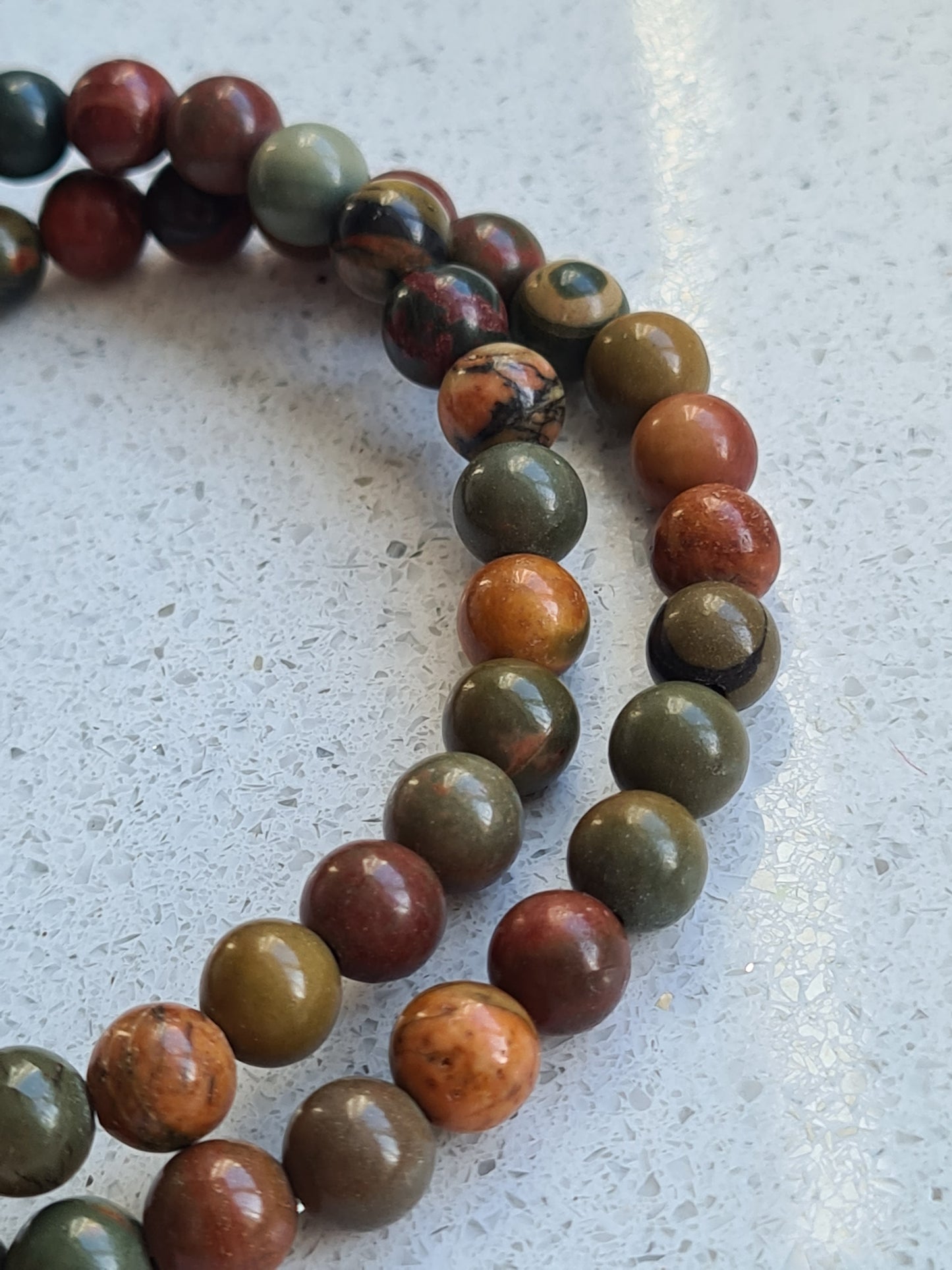 Natural Picasso Jasper 6mm rounded bead elasticated bracelets. Beads in colours of green, orange and red. Shown on white quartz background.