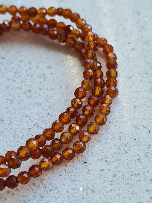 Three orange Hessonite garnet faceted bead bracelets on white granite background.