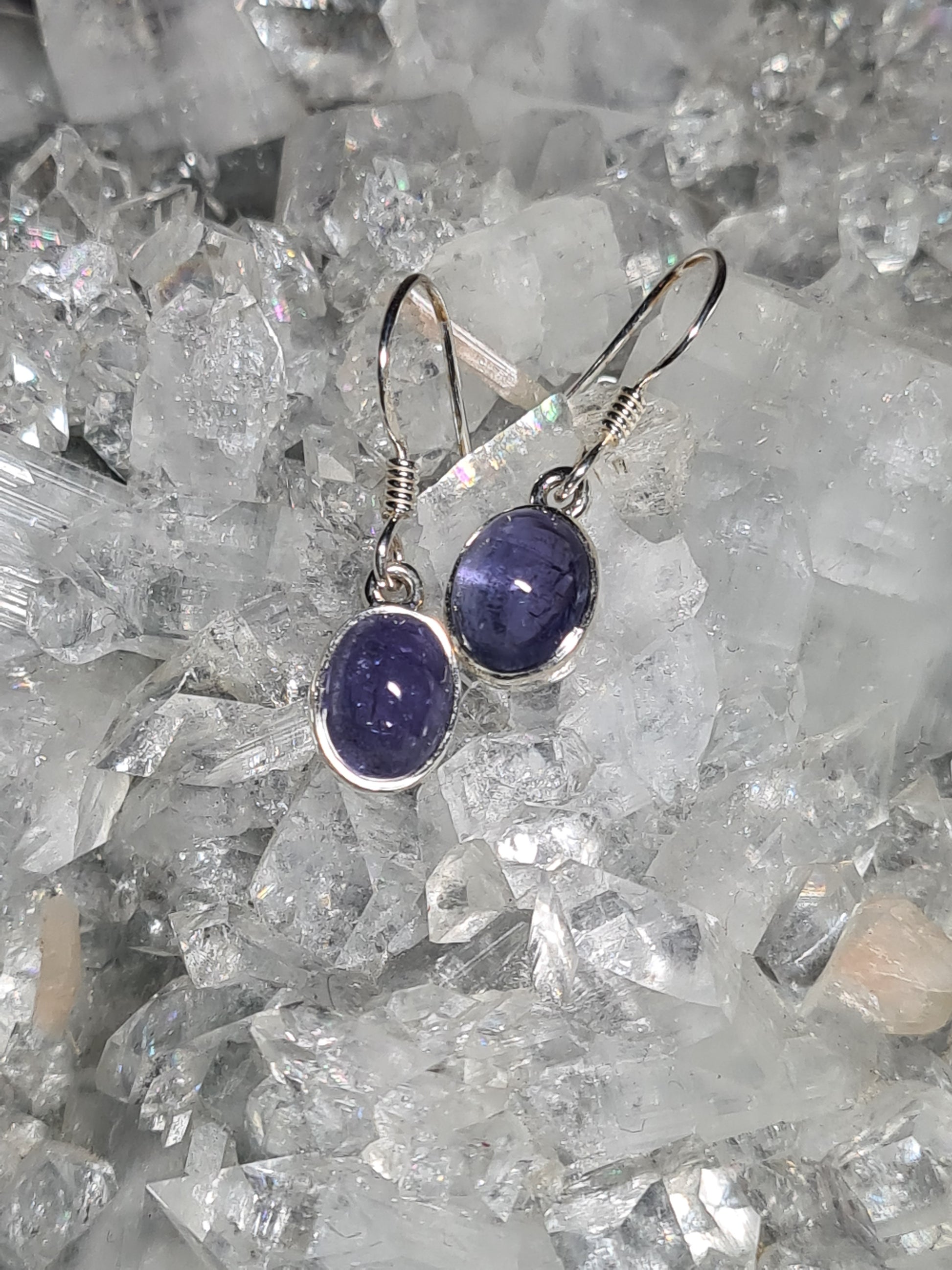 A pair of Natural Tanzanite set silver drop earrings, set with an oval cabochon blueish-violet tanzanite. Photographed on a crystal cluster.