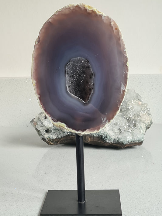 Large half grey banded agate geode with druzy quartz centre displaying unusual dendritic patterns. On fixed stand. 