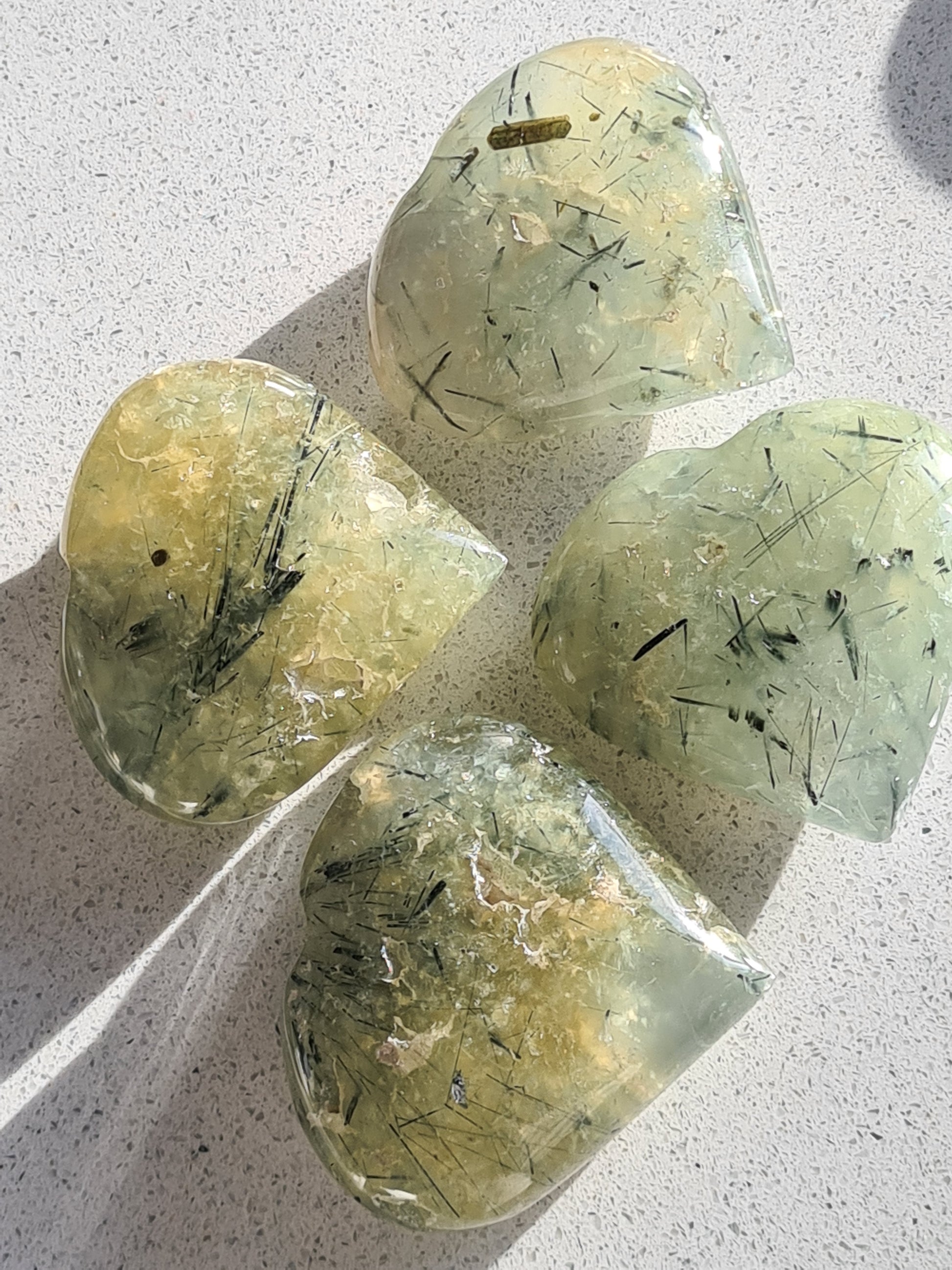 Natural Green Prehnite Carved Polished Heart Crystals with Epidote Inclusions. 
Four, photographed on a white quartz background in natural daylight.