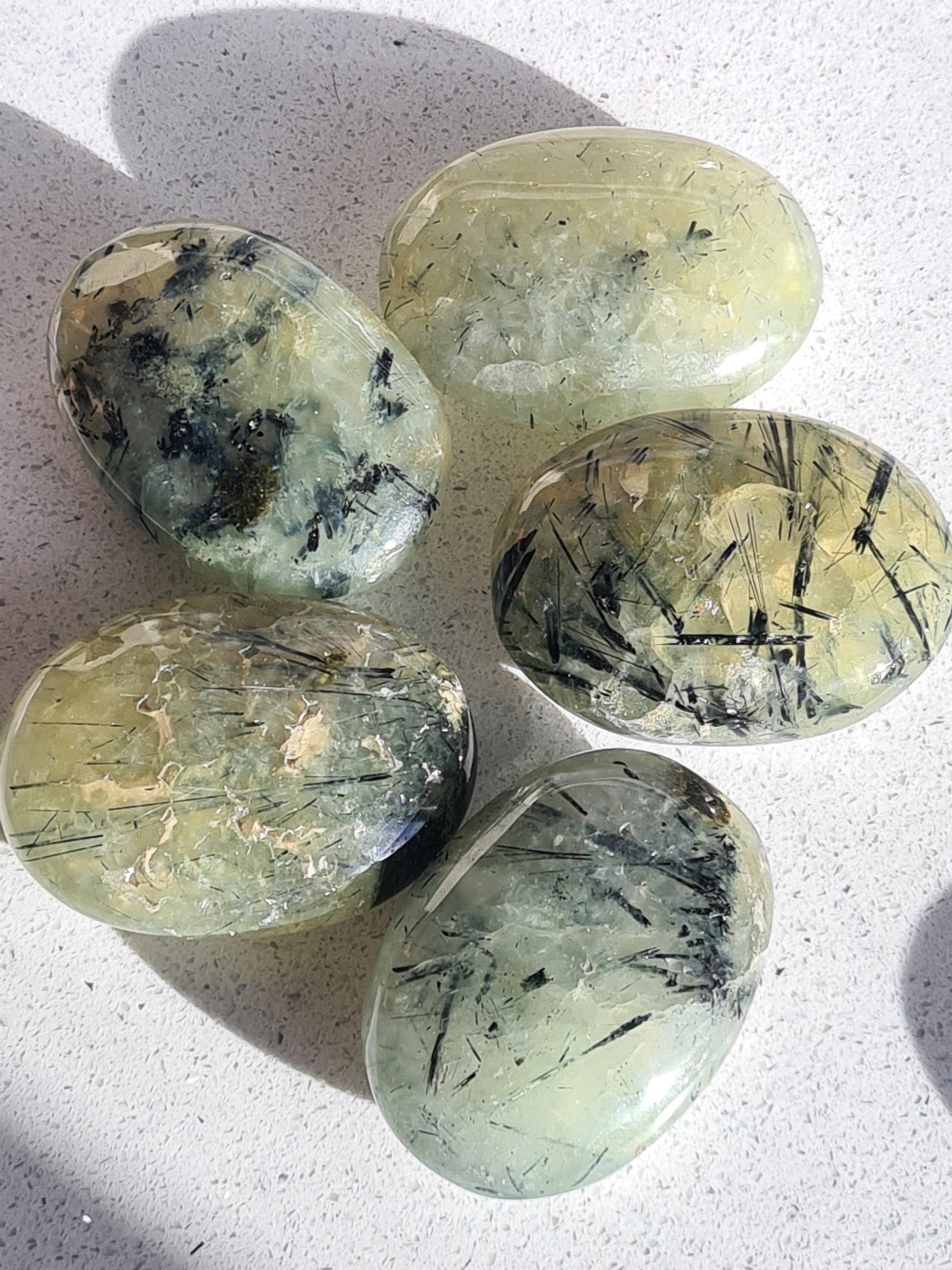 Natural Green Prehnite Oval Palmstones with Dark Green Epidote Inclusions. Each unique with varying amounts of Epidote. 
Five pieces photographed on a white granite background. 