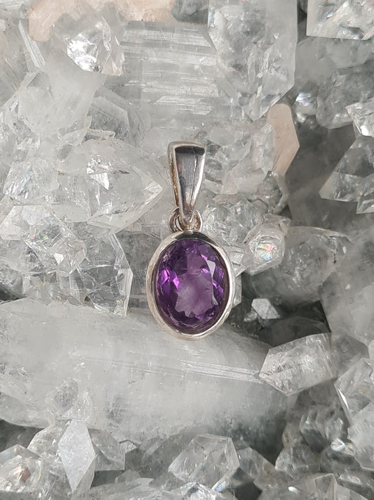 An oval shaped faceted purple amethyst pendant in sterling silver.
Photographed on an apophyllite raw cluster.